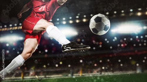 Close up of a soccer scene at night match with player in a red uniform kicking the ball with power © alphaspirit