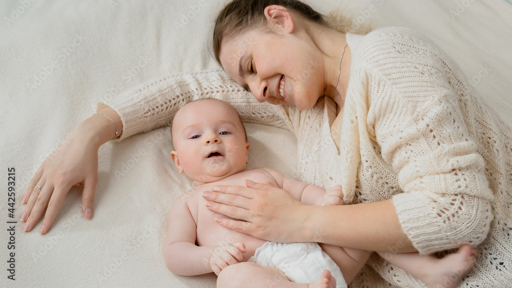 Little baby boy in diapers lying next to mother in bed. Concept of parenting ,baby care and family happiness Little baby boy in diapers lying next to mother in bed. Concept of parenting ,baby care and family happiness