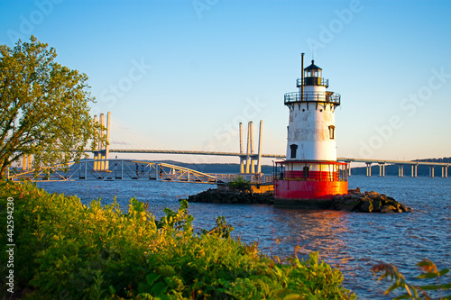 Short, red and white lighthouse on the Hudson River with a small bridge leading to it and a larger bridge further in the background -09