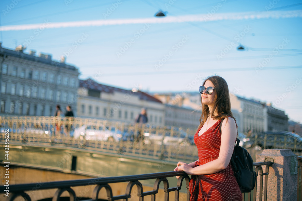 Portrait of a beautiful young woman on the embankment of the river at sunset in summer.