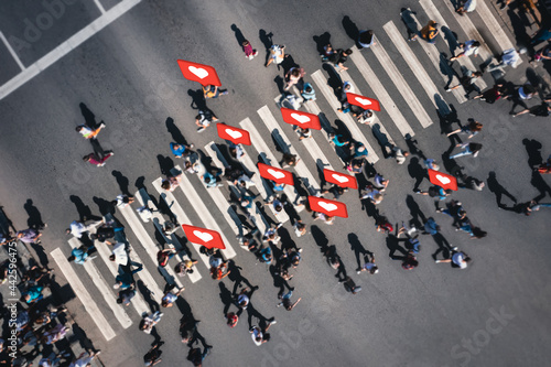 Different blurred people at a pedestrian crossing with social heart icons and likes in the city. People at a zebra pedestrian crossing - a lot of pedestrians in an overcrowded city on a sunny day.