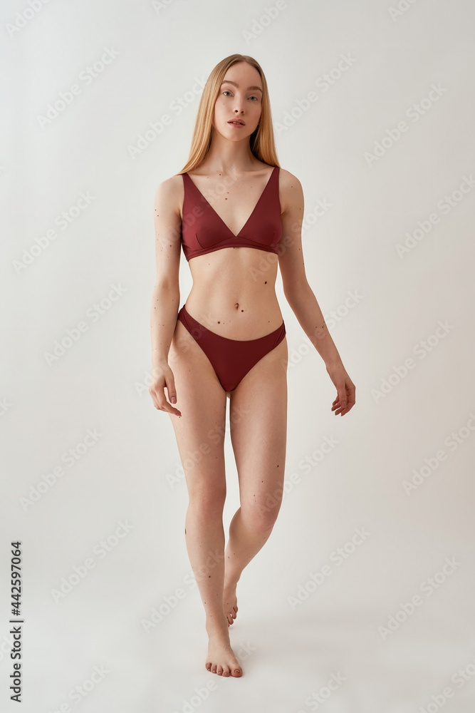 Full length shot of young slim caucasian woman with fit body wearing burgundy underwear looking at camera, posing isolated over light gray background Full length shot of young slim caucasian woman with fit body wearing burgundy underwear looking at camera, posing isolated over light gray background