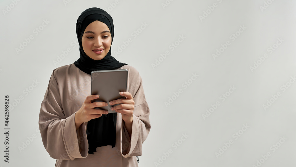Cute young arabic woman in hijab looking into tablet Cute young arabic woman in hijab looking into tablet
