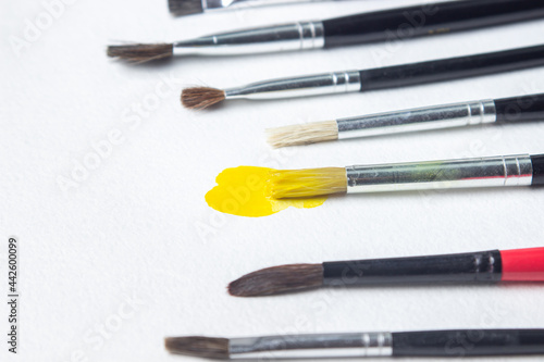 Paint brushes on a white background. One brush with yellow paint. Watercolor paint