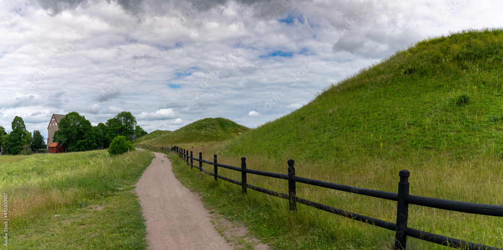 picturesque country landscape with a gravel path along grassy hills and a long brown wooden fence picturesque country landscape with a gravel path along grassy hills and a long brown wooden fence