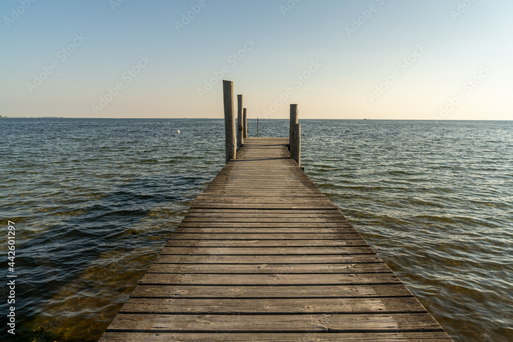 wooden dock leading out into a calm blue ocean in evening light
