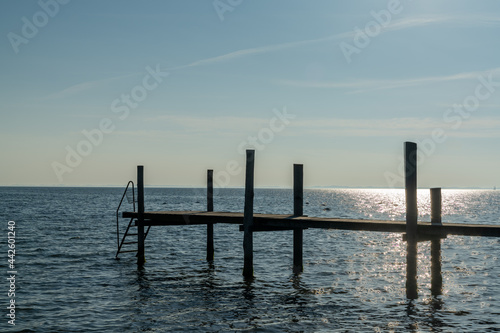 sunset over the ocean with a wooden dock and ladder for swimming in the foreground