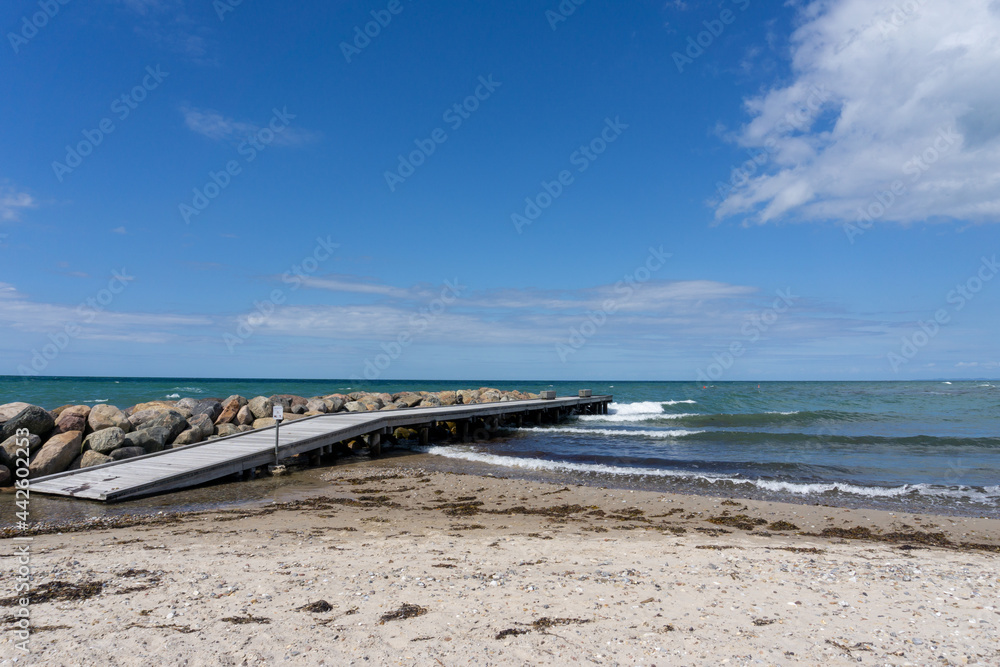 wooden dock and rocky storm groin lead out into the ocean from a sandy beach