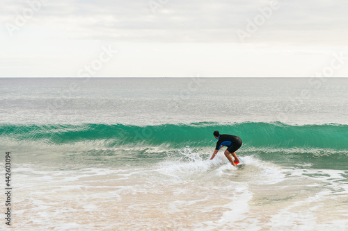 Caucasian hispanic man surfing on a skimboard next to a wave at sunset on the beach
