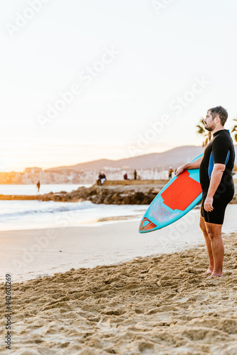Caucasian hispanic man standing on the beach at sunset with a skimboard clutched in his hands