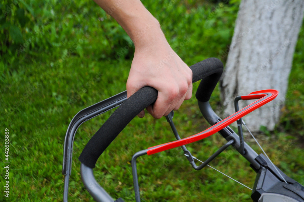 Man mowing the lawn with a lawn mower. Close up on the hands holding the device in the garden Man mowing the lawn with a lawn mower. Close up on the hands holding the device in the garden