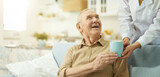 Smiling senior citizen looking at her nurse and going to drink a hot drink at home