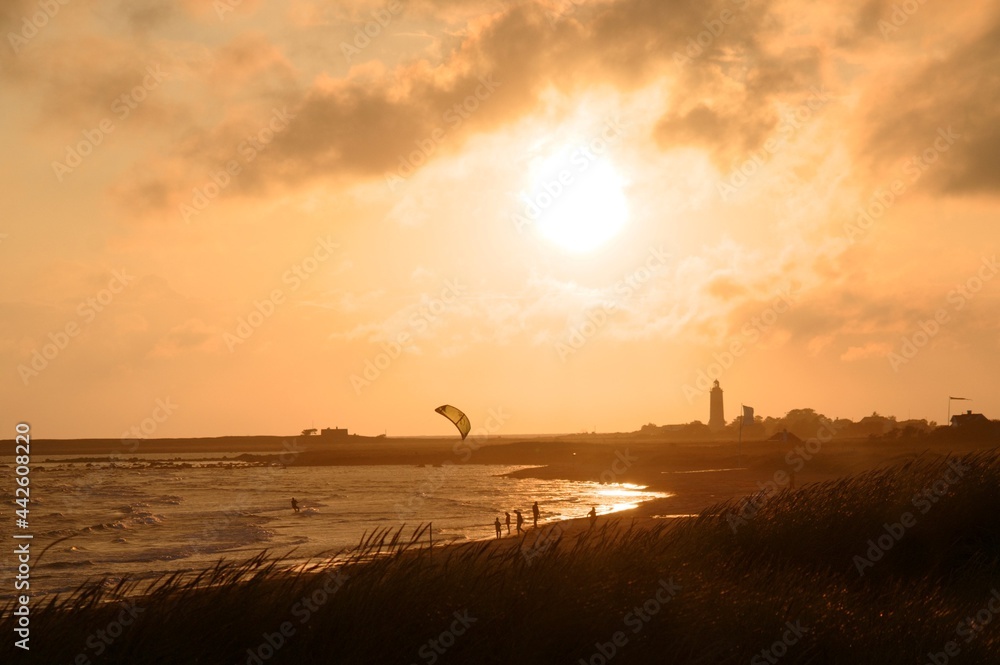 Beautiful sunset moment on the beach with wind kite surfing and people walking on the beach. Lighthouse in the background