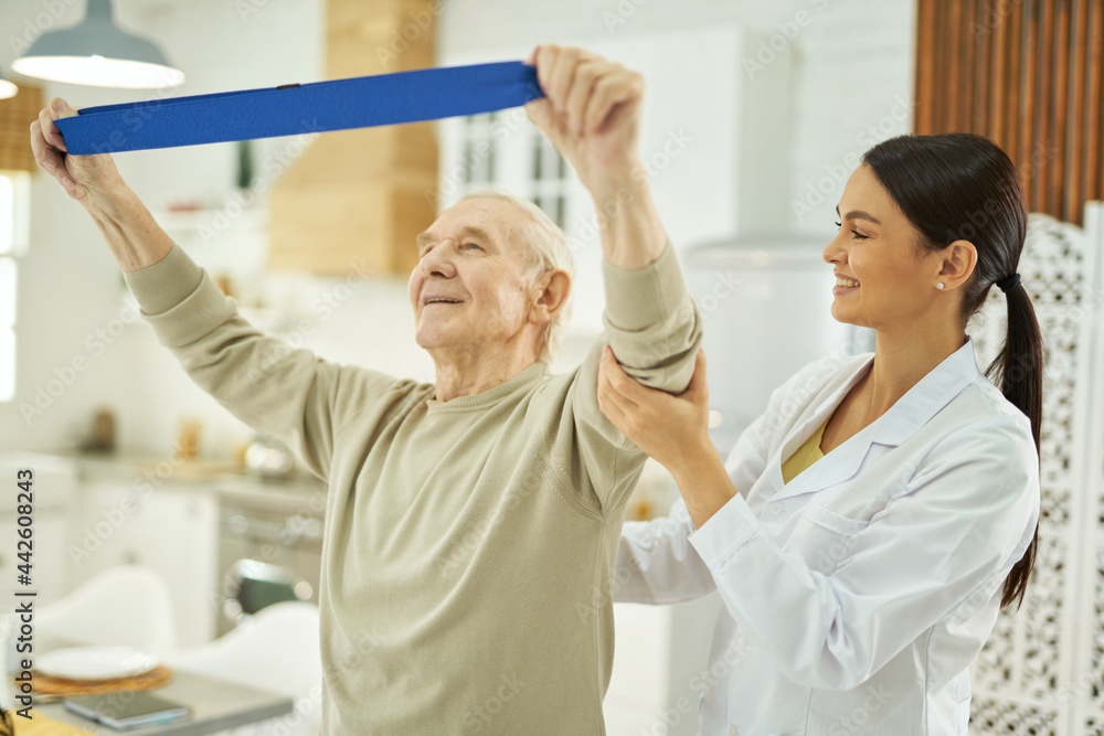Fototapeta premium Smiling pretty nurse helping an elderly man to do exercises at home