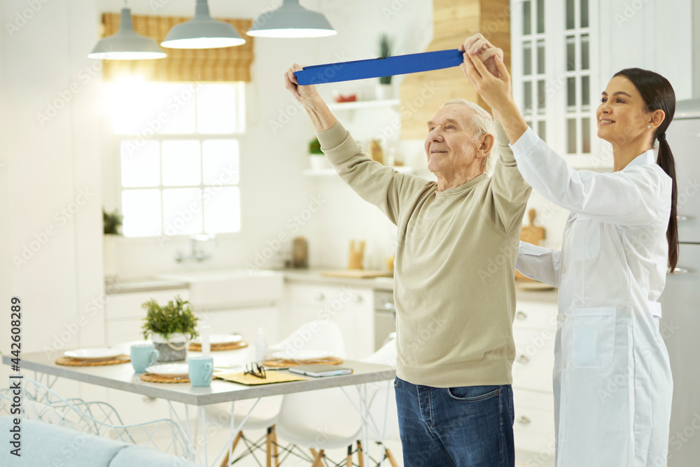 Fototapeta premium Thoughtful young nurse helping an elderly man to do exercises at home