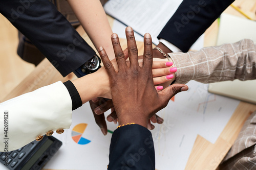 The black leader's hand covers the hands of the business team. A circle from the hands of multiethnic people working together in the office. Leadership and team concept