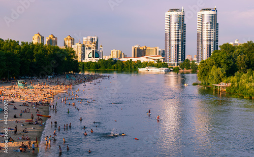 View from the bridge to the river and the beach in the city. Two twin houses away. A lot of people swim in the water and relax on the sand. women, men and children. UKRAINE, KIEV, JUNE, 2021