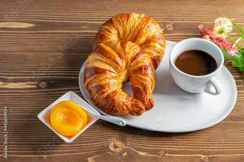 French fresh croissants, peach jam and a cup of black coffee on the wooden table. Country morning breakfast, top view at an angle.