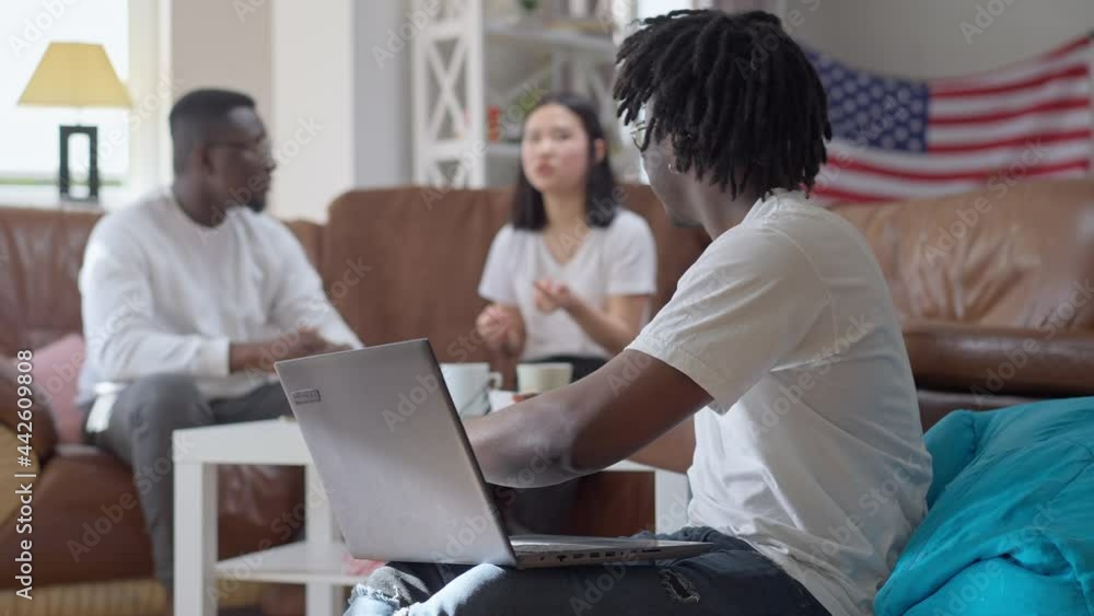 Happy handsome young man rejoicing startup success talking to blurred friends at background. Smiling cheerful African American startuper making victory gesture boasting success Happy handsome young man rejoicing startup success talking to blurred friends at background. Smiling cheerful African American startuper making victory gesture boasting success