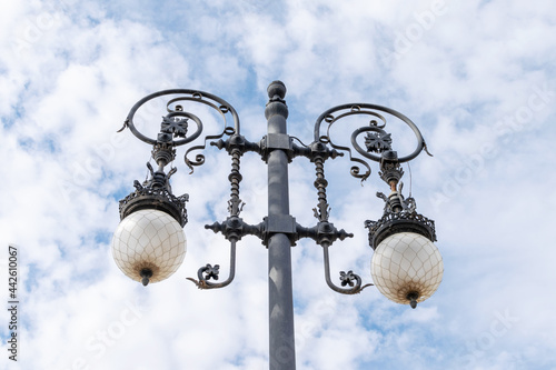Detail of metallic street light on the blue sky with white clouds background. Antique metallic street light details.