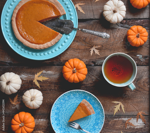 Overhead view of pumpkin pie and cup of tea surrounded by mini pumpkins on rustic wooden table