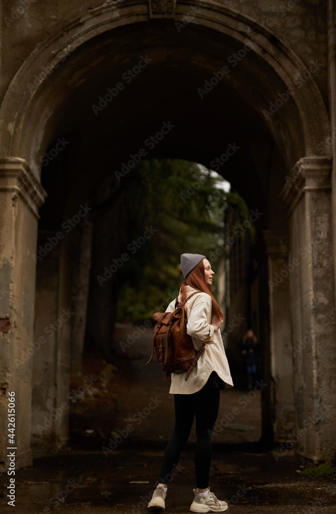 rear view on traveler woman with backpack stand in historical ancient arch, exploring interesting old sites and attractions, historical places, at autumn or spring season. view from back.