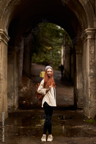 woman with backpack stand in historical ancient arch, exploring interesting old sites and attractions, at autumn or spring season. view from back on female turned and looking at camera © alfa27