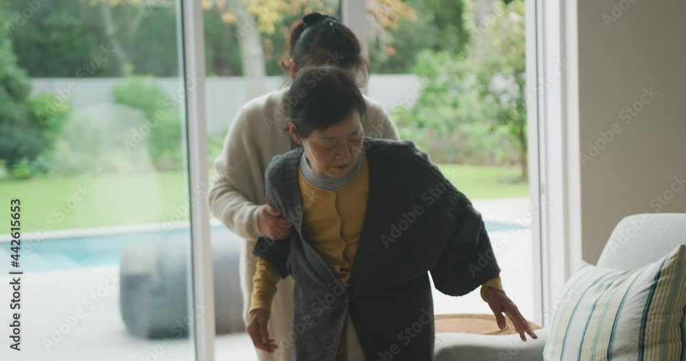 Senior asian mother being helped to armchair by adult daughter in living room Senior asian mother being helped to armchair by adult daughter in living room
