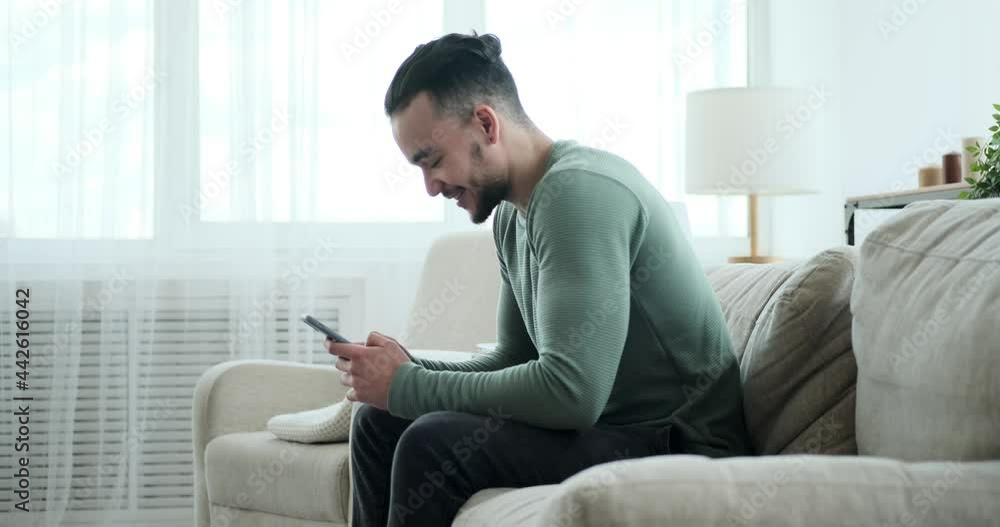 Handsome man text messaging using mobile phone on sofa at home Handsome man text messaging using mobile phone on sofa at home