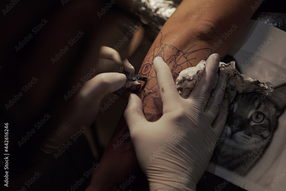 © ADDICTIVE STOCK - Crop master making tattoo on arm of client