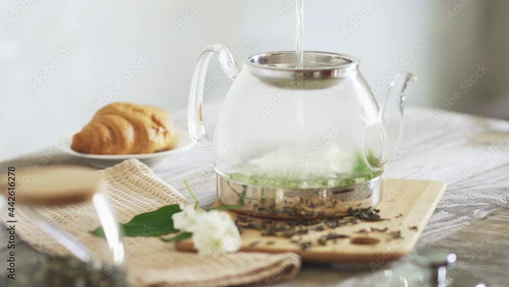 Pour hot water over jasmine flowers in teapot. Brew jasmine tea in transparent glass teapot. Pouring jasmine tea on a sunny morning. Cooking green tea croissant in the background. Hot drink concept.
Pour hot water over jasmine flowers in teapot. Brew jasmine tea in transparent glass teapot. Pouring jasmine tea on a sunny morning. Cooking green tea croissant in the background. Hot drink concept.