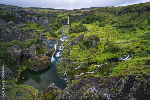 Gjain watrfall cascade, colorful lava rocks valley, lush green moss and vegetation and blue water streams in south Iceland photo