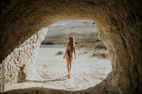 Anonymous woman in swimwear standing near stony cave photo