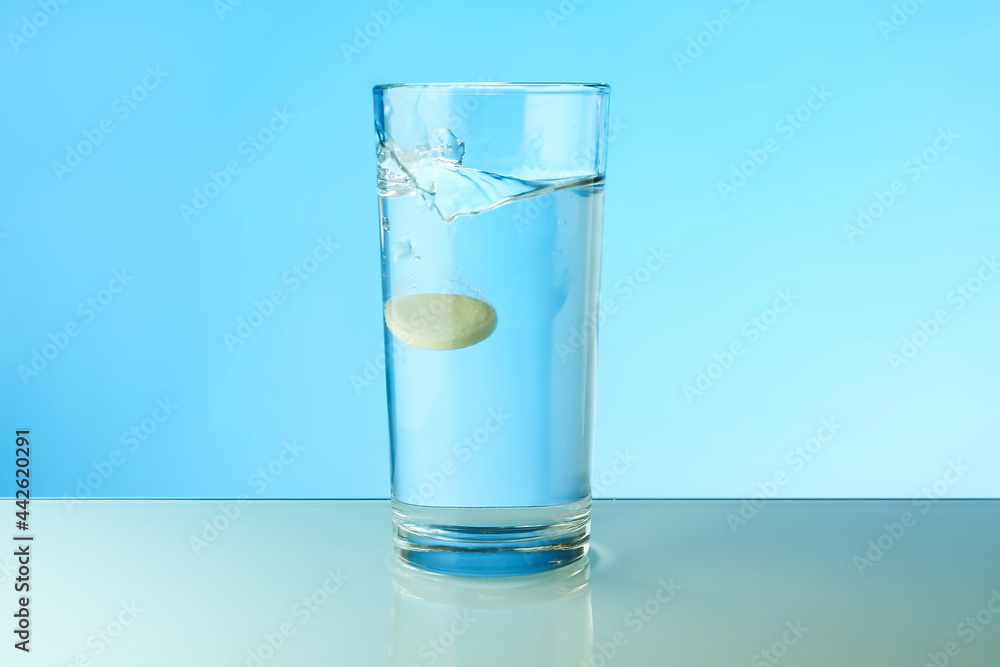 dissolving tablet dissolves in water on colored background. a glass of