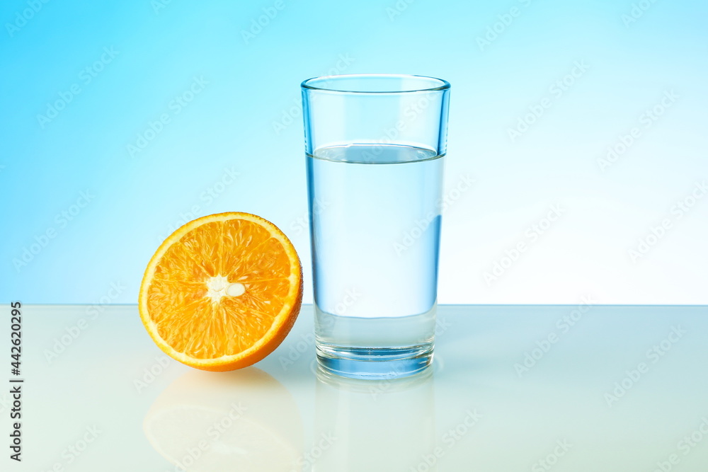 a glass of water and half of orange on blue background with copy space. vitamin C concept. a glass of water and half of orange on blue background with copy space. vitamin C concept.