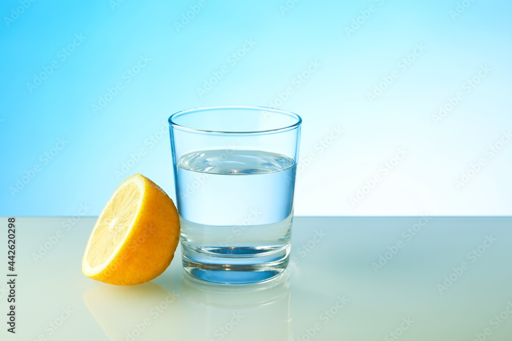 glass of pure water and half of lemon on blue background with copy space. vitamin C concept. glass of pure water and half of lemon on blue background with copy space. vitamin C concept.
