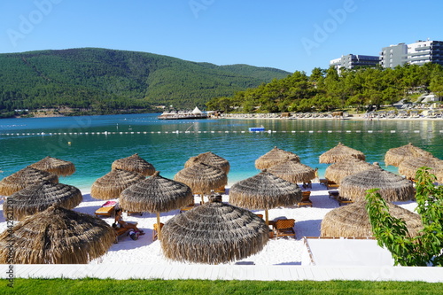 Fototapeta Naklejka Na Ścianę i Meble -  Bodrum, Turkey - August, 2020 Hotel Lujo, Beautiful Aegean sea turquoise blue color and palm trees on the beach. Sun loungers and umbrellas for tourists, Lux tourism concept 