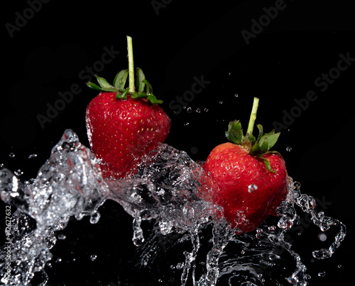Fresh strawberries in the air water splash on black background