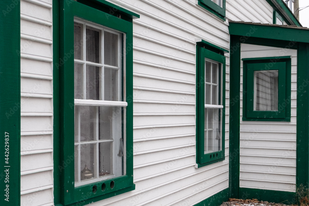 Fototapeta premium A vintage style one and a half story building. The vernacular structure is clad in cape cod clapboard with multi-panes and a number of single hung windows. The white building has green trim.