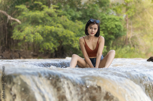 A woman short hairs in short pants and waistcoat on nature water and waterfall , she enjoy and relax time in weekends