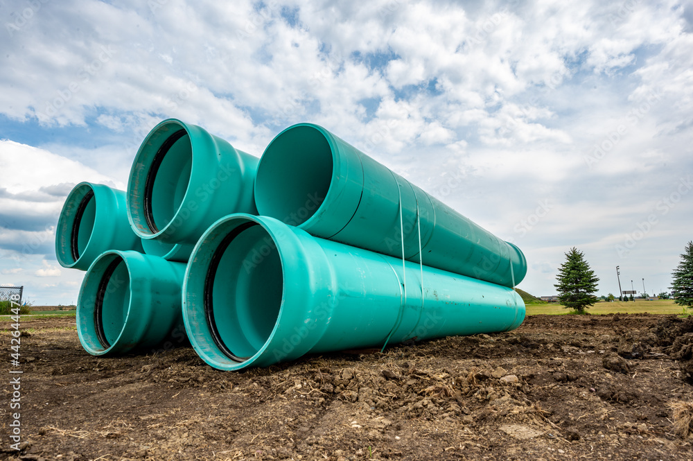 Stacked water main pipe with bell fitting next to an exposed trench for installation Stacked water main pipe with bell fitting next to an exposed trench for installation