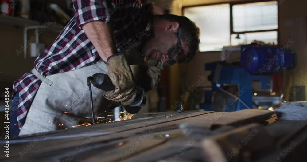Caucasian male knife maker in workshop wearing glasses and using angle grinder Caucasian male knife maker in workshop wearing glasses and using angle grinder