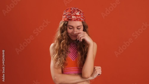 The embarrassed curly-haired woman with bandana on her head looking down in the orange studio photo