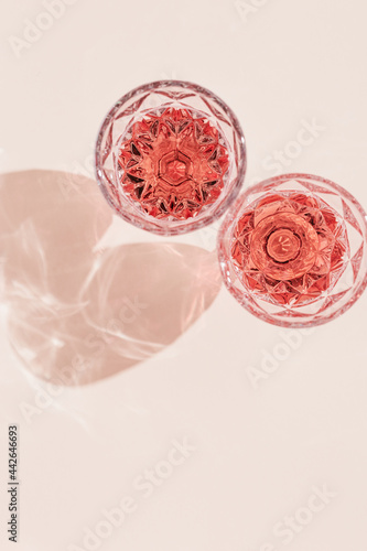 Two glasses of rose sparkling wine top view, fashion glass with beautiful pattern with dark shadows on pastel pink background.