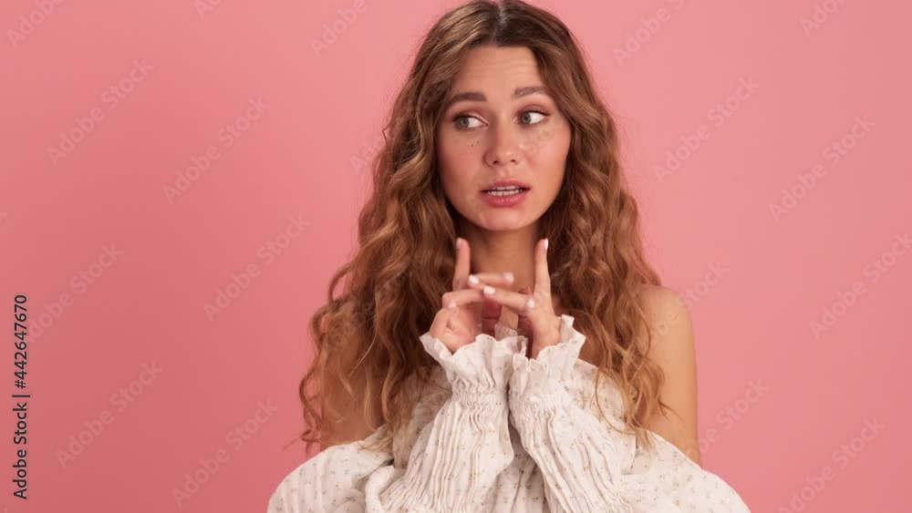 A curly-haired woman in a lace dress fingering and showing shh gesture in the pink studio A curly-haired woman in a lace dress fingering and showing shh gesture in the pink studio