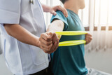 A physiotherapist is helping a patient stretch his arm using cloth at the clinic.