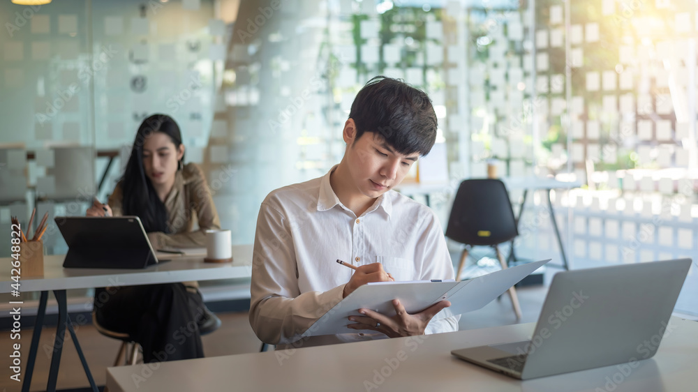Young Asian businessman holding document and taking notes at the office. Young Asian businessman holding document and taking notes at the office.