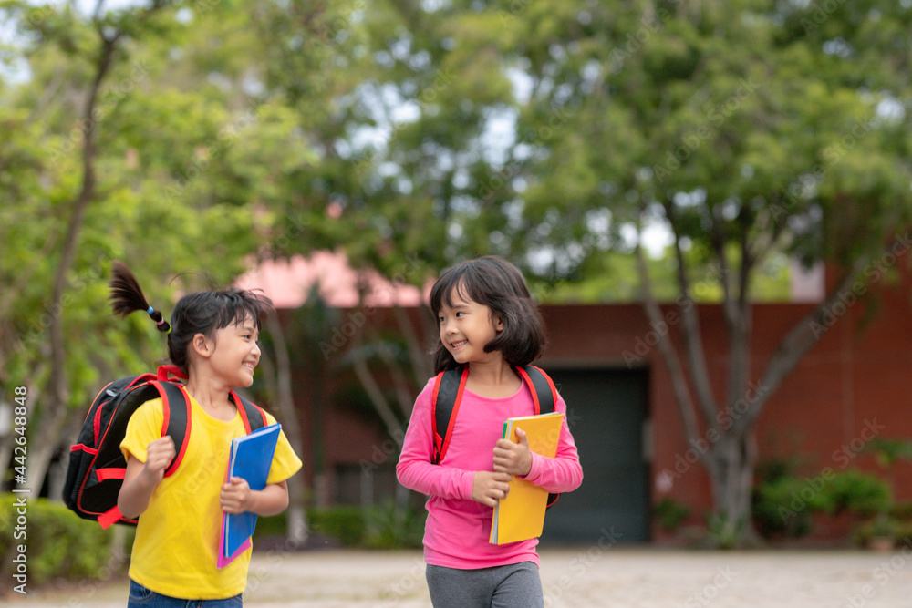 Obraz premium Back to school. Two cute asian child girls with school bag holding book and walk together in the school