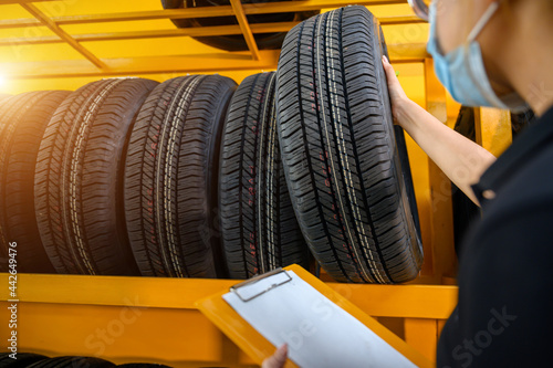 A young woman worker with a clipboard checking stocks of new tires ready to be replaced at a service center or tire shop. The background is a warehouse. Stock new tires for the car industry.