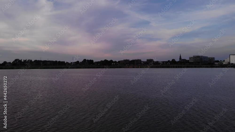 Birds Flying Over Quiet River With Silhouetted Coastal City Against Colorful Sky At Crezeepolder, South Holland, Netherlands. - Aerial Shot Birds Flying Over Quiet River With Silhouetted Coastal City Against Colorful Sky At Crezeepolder, South Holland, Netherlands. - Aerial Shot